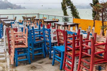 Fototapeta na wymiar Wet wooden tables and colorful chairs under the rain. Istanbul