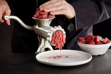 Cook in black uniform mincing meat with grinder