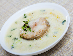 Boiled creamy soup with white fish pollock and greens at plate