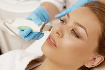 Naklejka premium Cropped close up of a beautiful young woman having ultrasound cleansing treatment facial procedure by professional cosmetologist at beauty salon spa center skincare youth pampering smooth ultrasonic
