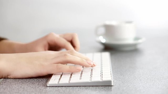 Closeup video of female hands, typing on the PS keyboard, at the table in the office. cup of coffee background