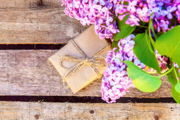 Floral decor elements. Small gift box with presents wrapped craft brown paper with bouquet of flowers beautiful smell violet purple lilac in vase on rustic wooden background. Copy space