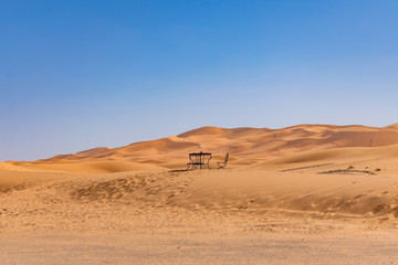 Fototapeta na wymiar Table and Chair in the distance on a Sand Dune in the Sahara Desert