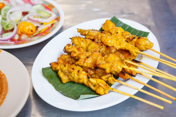 appetizer dish of traditional Thai street food recipe, Pork Satay Grilled pork stick putting on banana leaf in white plate served with sweet peanut dipping sauce and vinegar. Thailand Asia Food Travel