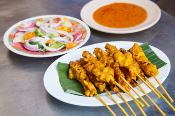 appetizer dish of traditional Thai street food recipe, Pork Satay Grilled pork stick putting on banana leaf in white plate served with sweet peanut dipping sauce and vinegar. Thailand Asia Food Travel