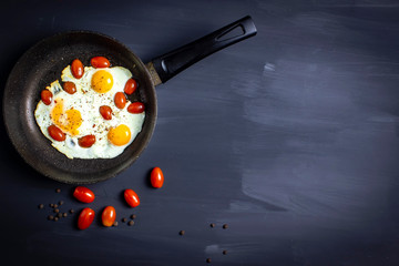 breakfast with eggs and tomato in a pan on dark background, top view
