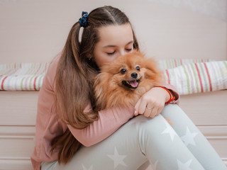 Teenage girl with a dog breed Spitz rejoices with a pet at home on the floor.
