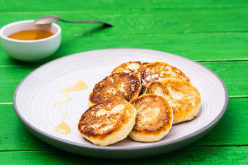 Homemade cottage cheese pancakes with honey on a plate on a wooden table