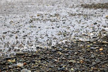 Pebbles on a sandy beach, shiny wet stones and waves.