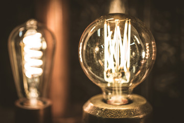 Vintage stylized round tungsten lamp glowing in dark, close-up photo with selective focus and...