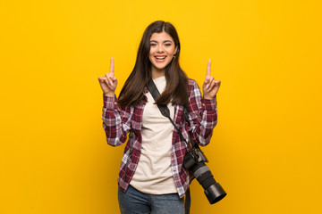 Photographer teenager girl over yellow wall pointing with the index finger a great idea