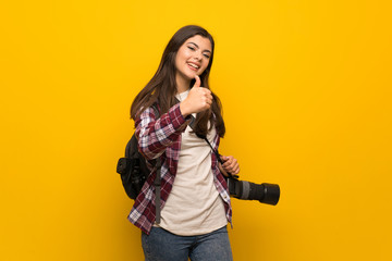 Photographer teenager girl over yellow wall with thumbs up because something good has happened