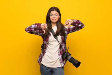Photographer teenager girl over yellow wall showing thumb down