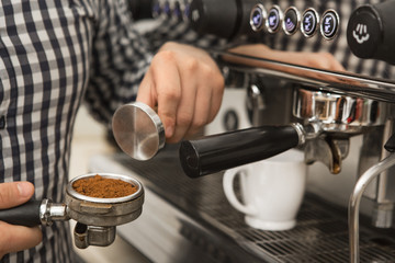 Cropped shot of a professional barista standing near coffee machine at his cafe preparing coffee holding a tamper and portafilter with pressed ground coffee profession occupation hipster worker job