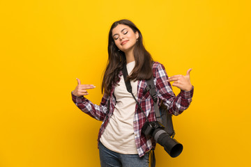 Photographer teenager girl over yellow wall proud and self-satisfied