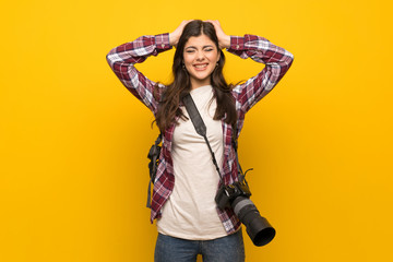 Photographer teenager girl over yellow wall frustrated and takes hands on head