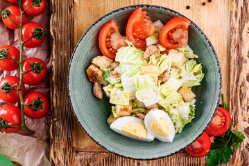 Caesar salad with chicken fillet, iceberg salad, egg, cherry tomato, white toast and parmesan cheese in a gray plate on a wooden board in a rustic composition. close up. flat lay