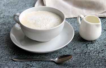 cup of coffee with crema, napkin, milk jug and spoon on gray background