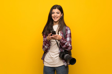 Photographer teenager girl over yellow wall sending a message with the mobile