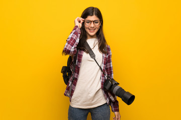 Photographer teenager girl over yellow wall with glasses and surprised