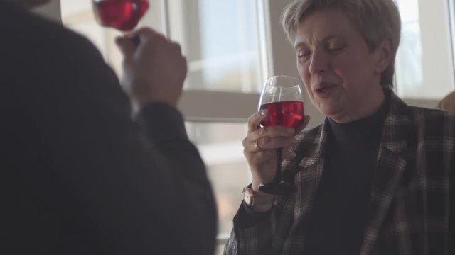 Back of man with glass of red wine and portrait of happy smiley senior woman with grey short hair with glass of wine. Couple talk and enjoy time together. Happy family.