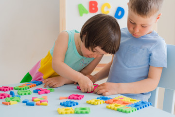 A boy and a girl collect a soft puzzle at the table. Brother and sister have fun playing together in the room.