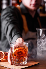 bartender serves beautiful cocktail with Sicilian orange in a transparent glass in the smoke. cocktail on the bar.  space. close up