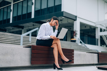 Asian businesswoman in eyeglasses using laptop working about business and finance feeling stressful- headache sitting in front office background- woman office worker and businesswoman concept