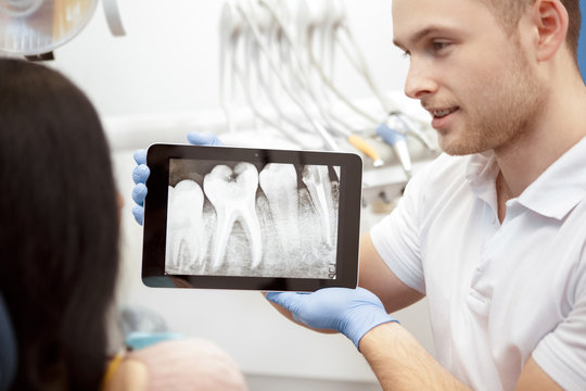 This is the issue. Handsome male dentist using digital tablet while working with his client showing x-rays on the display consultation problems operation dental surgery technology modern dentistry 