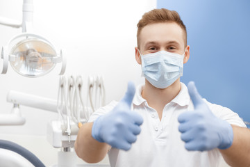 Immer professionell! Professioneller Zahnarzt mit Schutzmaske und Handschuhen, der in seiner Zahnklinik Kopienraum Professionalität Geste mit Daumen nach oben posiert