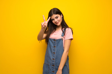 Teenager girl over yellow wall smiling and showing victory sign