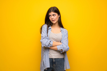 Teenager girl over yellow wall with confuse face expression while bites lip