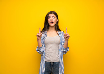 Teenager girl over yellow wall pointing up and surprised