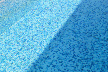 Fototapeta na wymiar Swimming pool bottom caustics ripple and flow with waves background. Surface of blue swimming pool, background of water in swimming pool. Clear light blue pool water ripples with sun reflections.