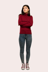 A full-length shot of a Teenager girl with turtleneck making doubts gesture while lifting the shoulders over isolated background
