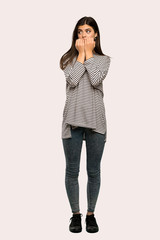 A full-length shot of a Teenager girl with striped shirt nervous and scared putting hands to mouth over isolated background