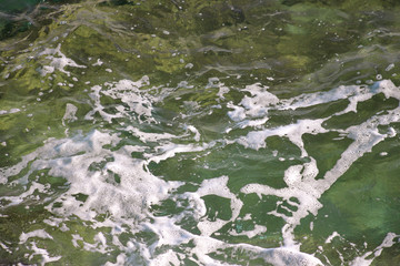 Turquoise green seawater with sea foam as background, close up. Surface of sea with waves, splash, foam and bubbles, blue abstract texture and wallpaper. Beautiful green waves with a lot of sea foam.