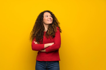 Fototapeta premium Teenager girl with red sweater over yellow wall looking up while smiling