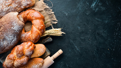 Assortment of bread and baking on a black stone background. Top view. Free space for your text.