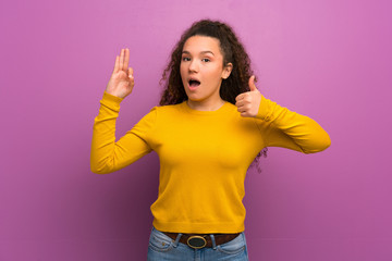 Teenager girl over purple wall showing ok sign and thumb up gesture