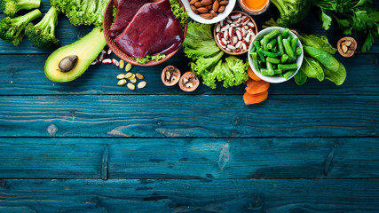 Food containing natural iron. Fe: Liver, avocado, broccoli, spinach, parsley, beans, nuts, on a blue background. Top view.