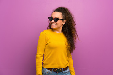 Teenager girl over purple wall with glasses and happy