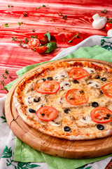Fresh italian pizza with mushrooms, chiken, tomatoes, cheese, olive on wooden board, red rustic table. Copy space. Homemade with love. Fast delivery. Recipe and menu. Top view.