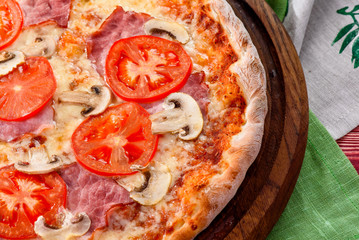Delicious italian pizza with ham, tomato and mushrooms served on wooden board. Red wooden background, decorated with napkins, chili pepper and cherry tomatoes. close-up. top view. flat lay