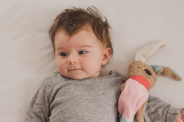 happy baby with bunny soft toy lying in bed
