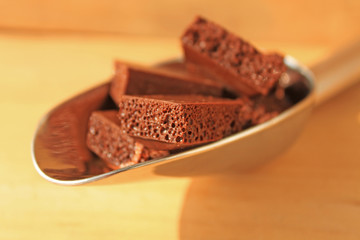 Milk porous chocolate in a steel scoop on a wooden background