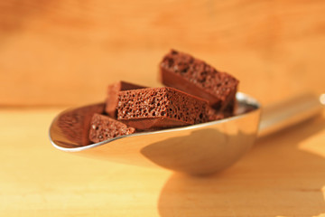 Milk porous chocolate in a steel scoop on a wooden background