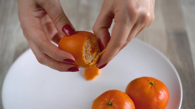 Women's hands peel the peel of tangerine, mandarin slices are piled on a plate