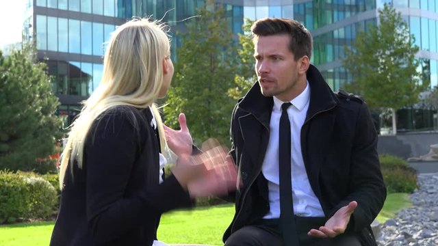 A businessman and a businesswoman sit on a bench and argue, he slaps her - an office building in the background