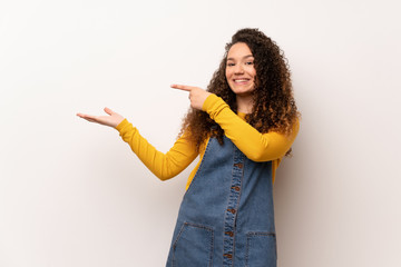 Teenager girl with red sweater over white wall holding copyspace imaginary on the palm to insert an...